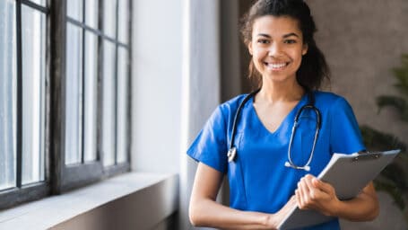African-american doctor working in hospital , healthcare and medical concept .Stethoscope around her neck. Female black doctor filling up medical form at clipboard while standing straight in hospital
