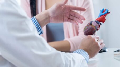 Male cardiologist gestures while discussing diagnosis with an unrecognizable female patient.