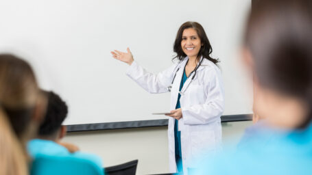 Doctor gestures to something on a whiteboard as she teaches a class at a medical school.