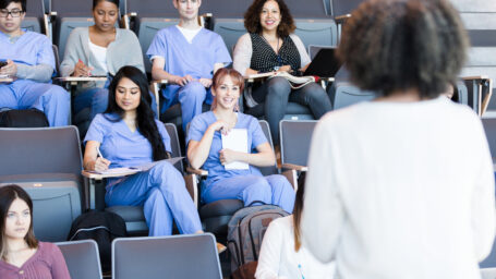 A class of attentive medical students listen to a mature female professor's lecture.